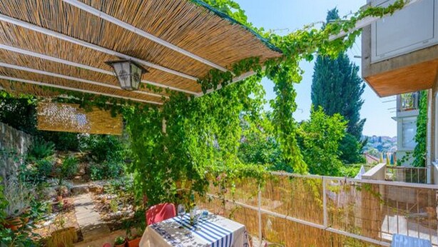 Eine Terrasssengestaltung im Freien mit Esstisch, umgeben von Kübelpflanzen und einem Bambuszaun.