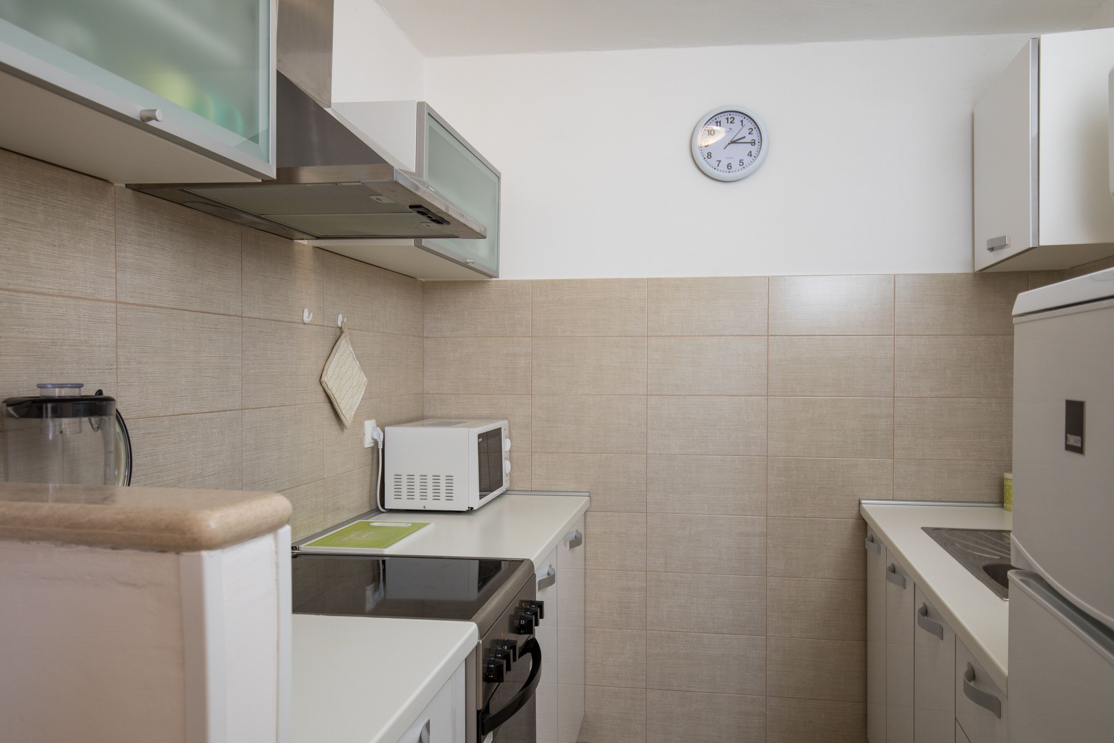 Une cuisine compacte équipée d’un four à micro-ondes, d’une cuisinière et d’un four. Une horloge est fixée au mur.