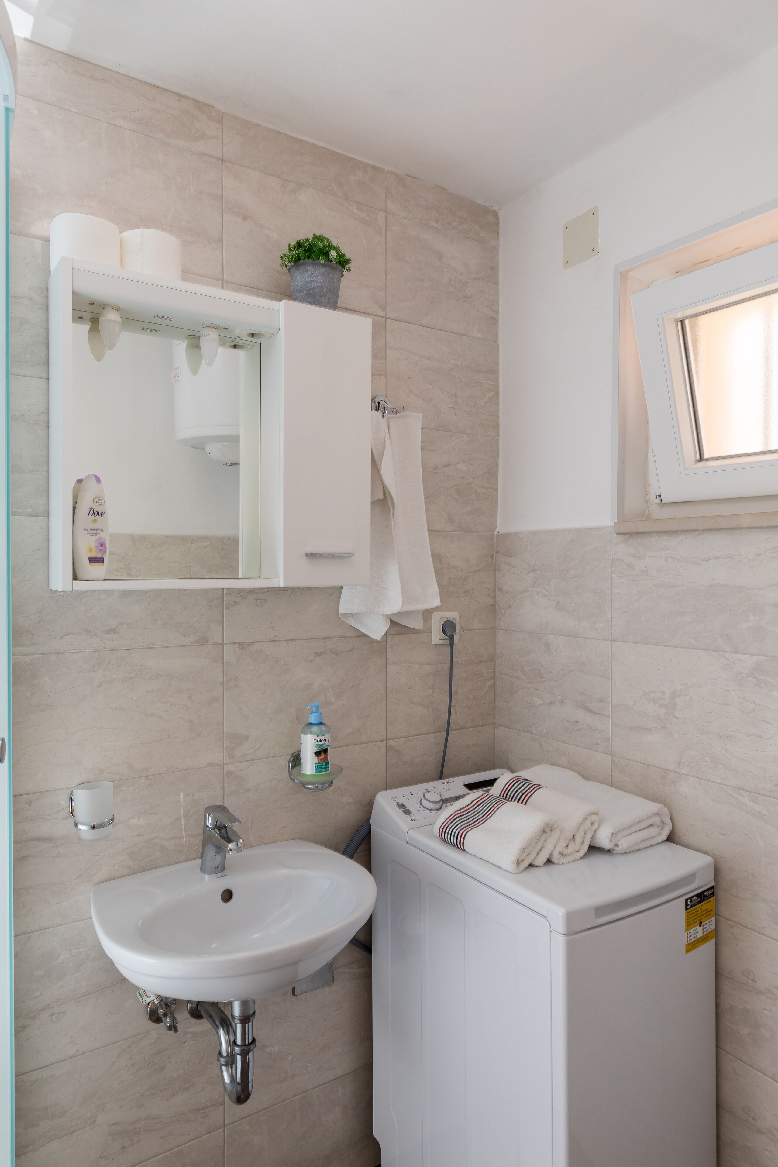 A bathroom with a sink, mirror, towel rack, and a washing machine.