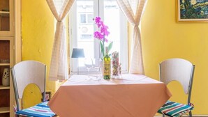 Un comedor con una mesa dispuesta para dos, sillas con cojines coloridos, un florero con flores y un cuadro en la pared.