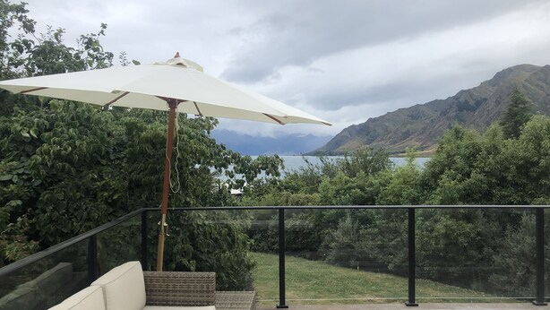 Een terras met een witte bank en een parasol, met uitzicht op een meer en bergen.