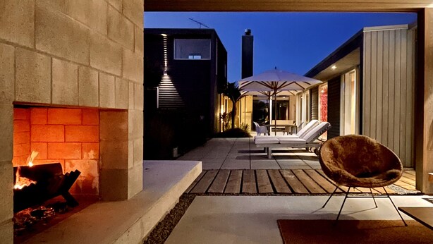 A modern outdoor patio with a fireplace, lounge chairs, and a dining area. - Award Winning Beach House - 100m from Beach (Omaha Beach)