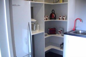 A compact kitchen with white cabinets, a red kettle, and a sink. - Miranda Sea View Apartment (Miranda)