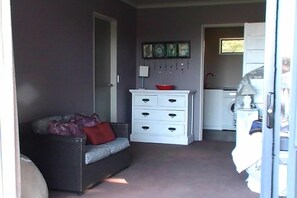 A room with a grey sofa, a white dresser, and a small kitchen area. - Miranda Sea View Apartment (Miranda)
