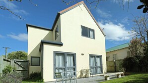 Una casa de dos pisos con techo plano, ventanas amplias y un patio con mobiliario exterior.