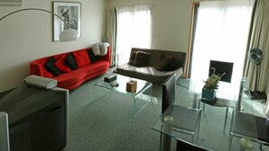 Ein modernes Wohnzimmer mit einem roten Sofa, einem grauen Sofa, einem Glastisch und einem Fernseher.