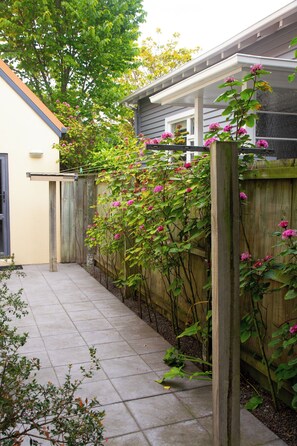 A residential backyard with a paved patio, a wooden fence, and flowering plants.