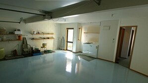 Una habitación amplia y vacía, con piso liso, paredes blancas y una puerta que da a otra estancia.