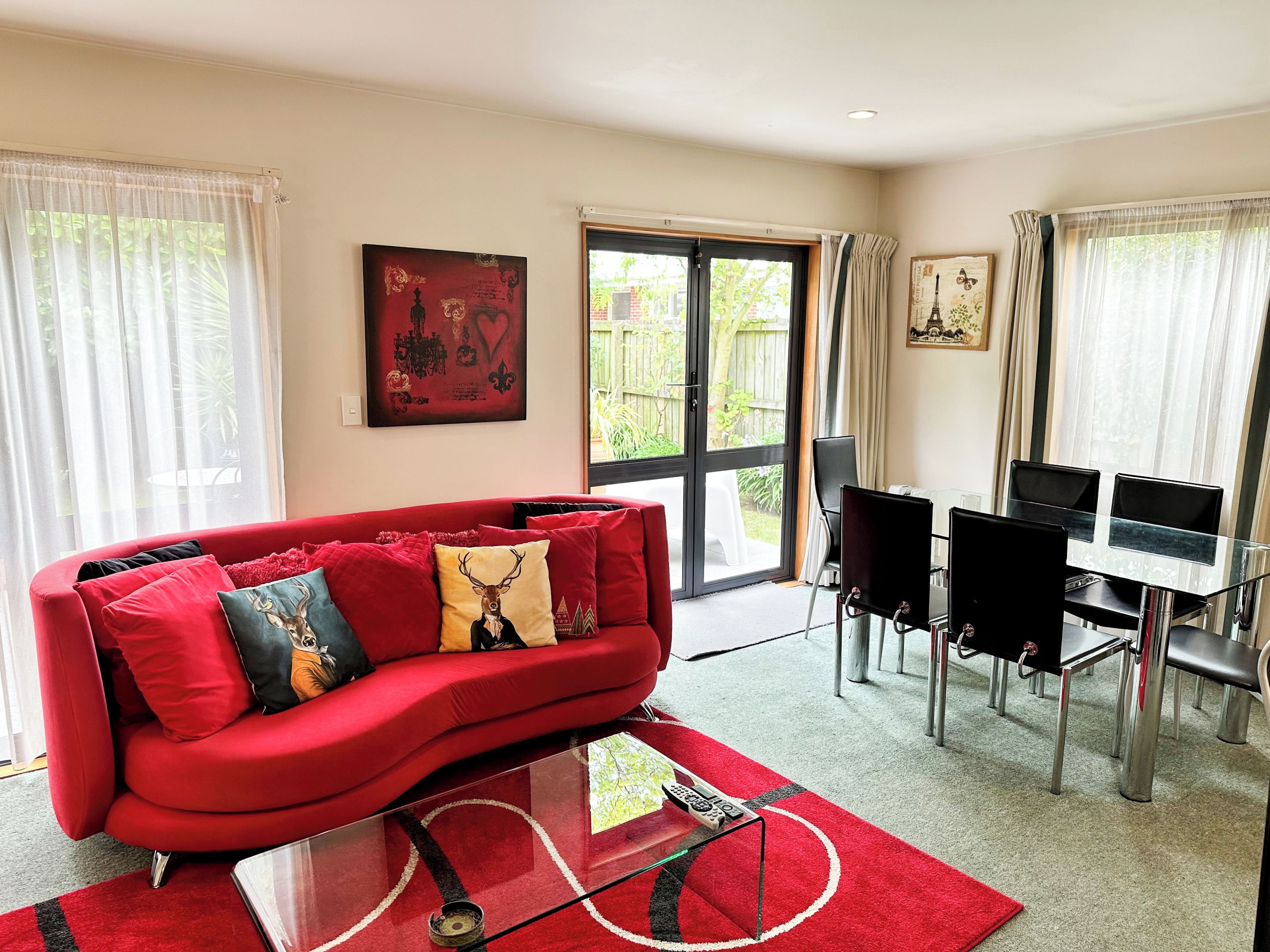 A modern living room with a red sofa, a glass coffee table, and a dining area with a glass table and black chairs.