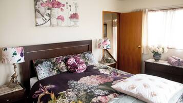 A bedroom with a bed, a nightstand, a lamp, a mirror, and a window with curtains.