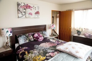 A bedroom with a bed, a nightstand, a lamp, a mirror, and a window with curtains.