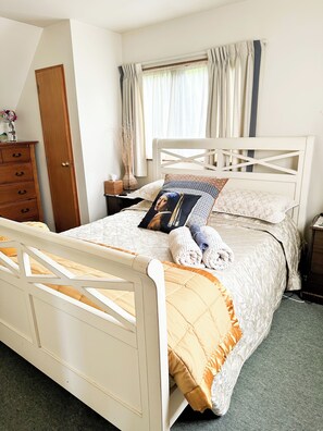 Un dormitorio con cama, cómoda de madera, mesita de noche y ventana con cortinas.