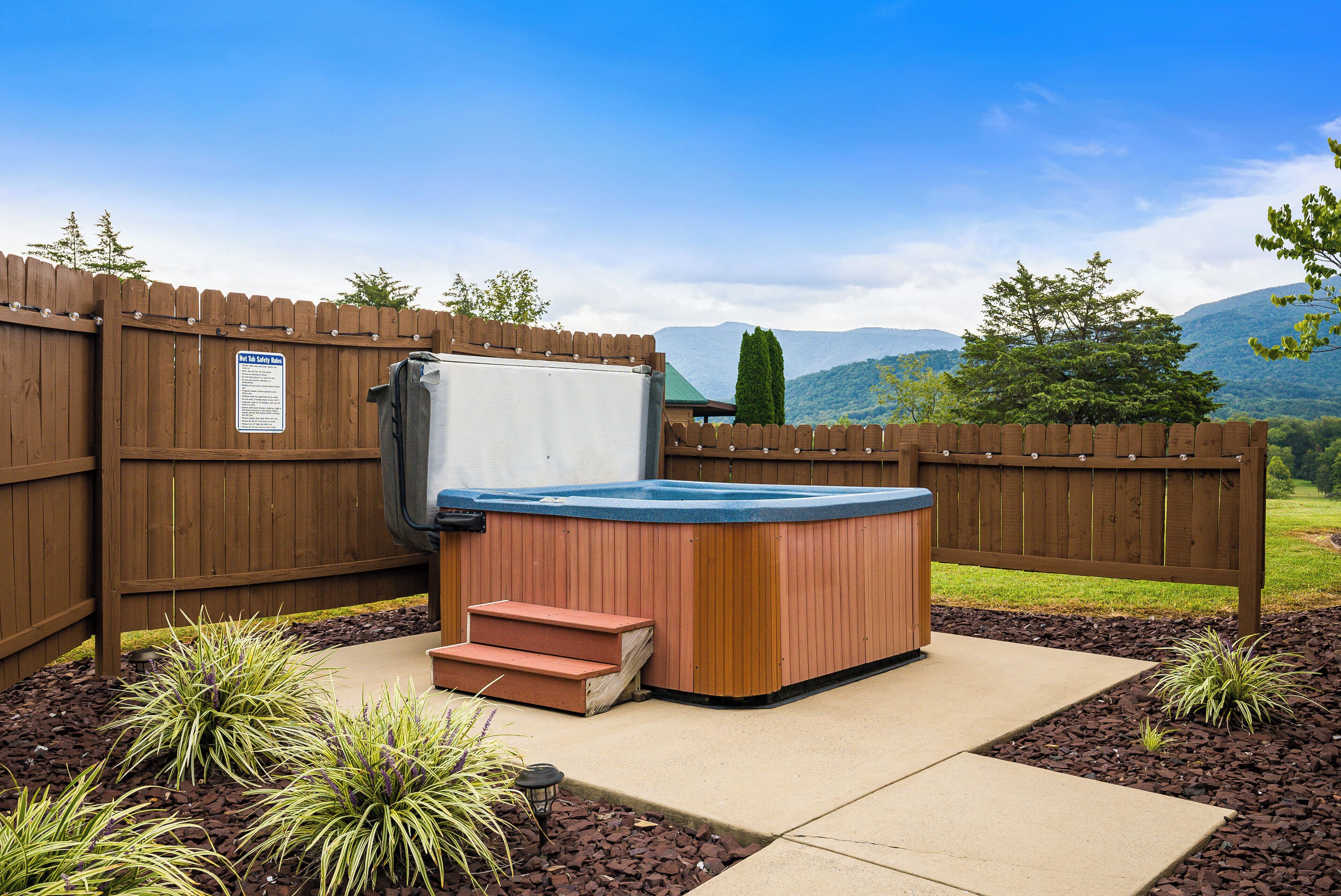 A hot tub with steps, surrounded by a wooden fence, with a mountain view in the background.