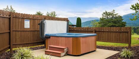 A hot tub with steps, surrounded by a wooden fence, with a mountain view in the background.
