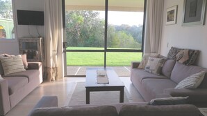 A living room with two sofas, a coffee table, and a TV on the wall. - Spacious, modern, tranquil, convenient, great location with sea views & bush.  (Tawharanui Peninsula)
