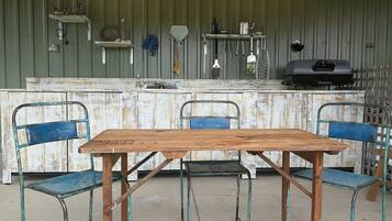 A rustic kitchen with a wooden table and chairs, a gas stove, and various kitchen utensils hanging on the wall.