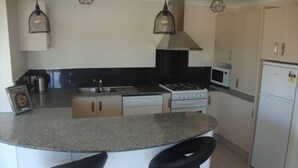 A modern kitchen with a granite countertop, stainless steel appliances, and bar stools.