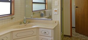 A bathroom with a beige sink, mirror, and two drawers. There is a window above the mirror and a door to the right. - Ngaio Beach House - Kaiteriteri-Marahau (Kaiteriteri - Mārahau)