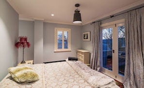 A bedroom with a bed, a dresser, a window with blinds, a door with curtains, and a ceiling light.