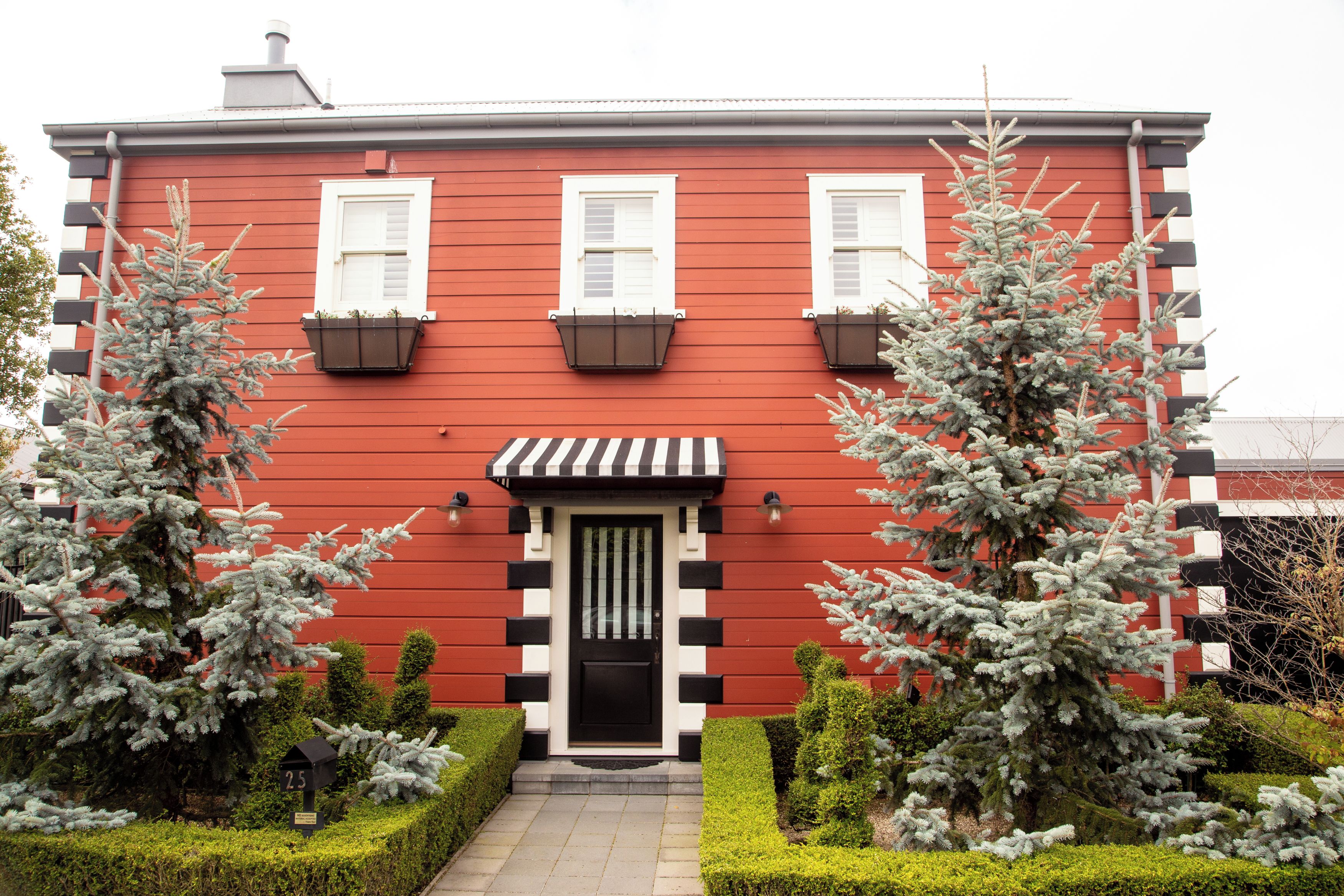 A red building with white shutters, a black door, and a small porch. There are two potted evergreen trees in front.