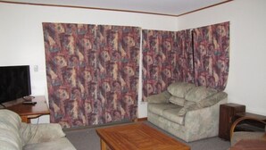 A living room with a sofa, armchair, wooden coffee table, and a television on a stand.
