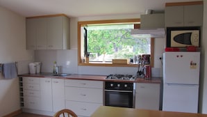 A compact kitchen with white cabinets, a wooden countertop, a gas stove, a microwave, and a window with a view of trees.