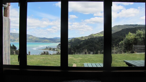 A room with a large window overlooking a scenic landscape including a lake, hills, and a picnic area.