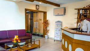 A hotel reception area with a reception desk, a purple sofa, a glass coffee table, and a plant. - Hotel Chennai Gate (Chennai)