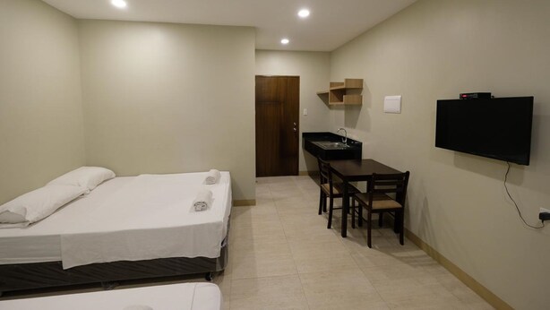 A hotel room with two beds, a desk, a TV, and a door leading to another room. - Kiwi South (Cebu City)