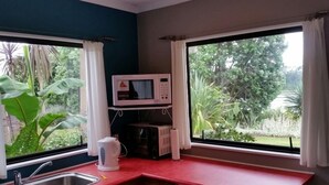 A compact kitchen with a red countertop, a microwave, a kettle, and a small refrigerator. - Estuary Edge - A Slice of Paradise (Te Puna)