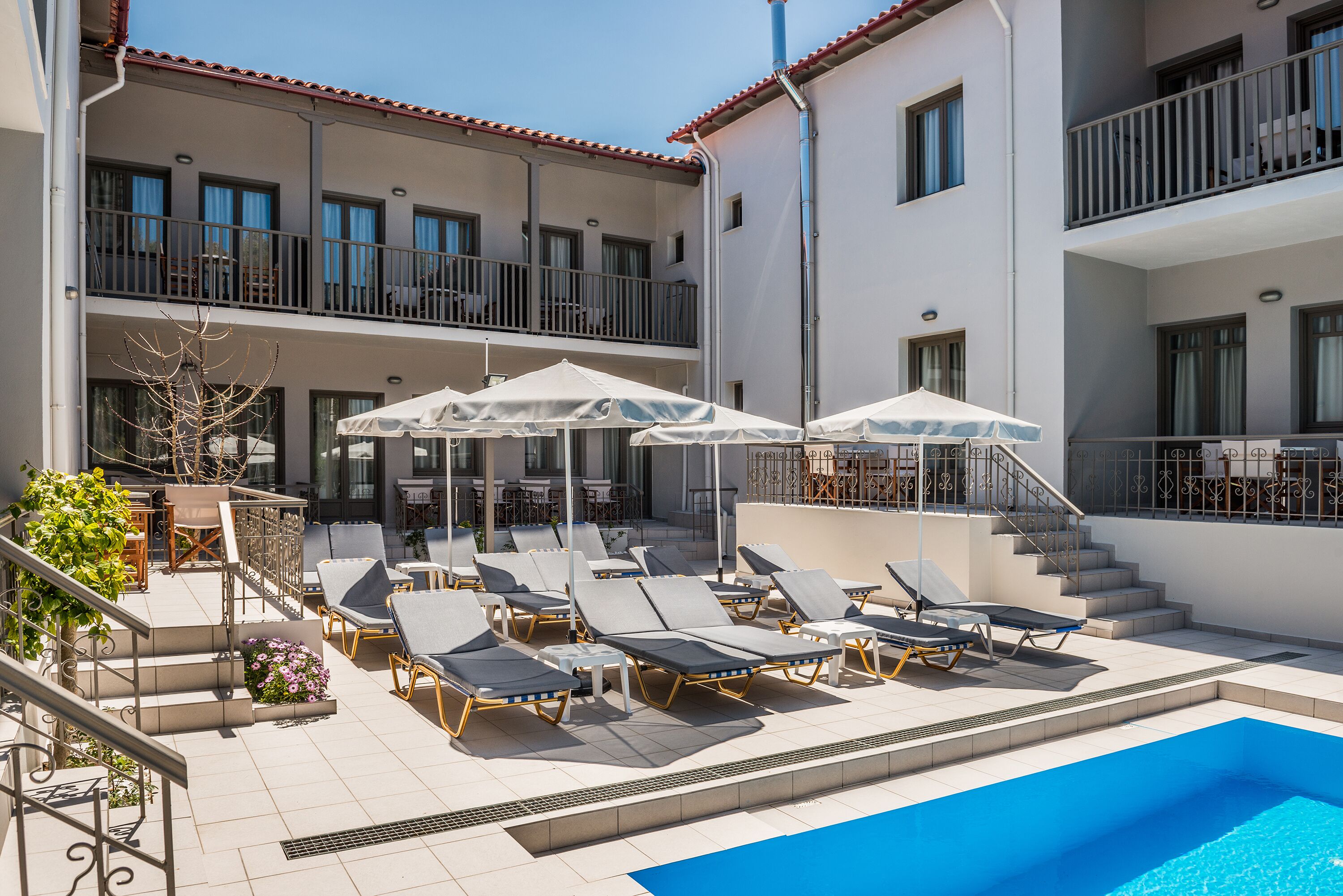 A rooftop pool area with sun loungers and umbrellas, a staircase, and a building with balconies.
