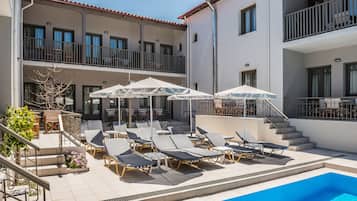 A rooftop pool area with sun loungers and umbrellas, a staircase, and a building with balconies.
