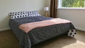 Una cama con colcha y almohadas estampadas con motivos de estrellas, una lámpara de noche y una ventana con vista a árboles.