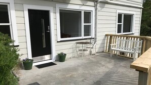 Una casa con puerta principal, dos ventanas, un pequeño patio con mesa y sillas, y un banco de madera.