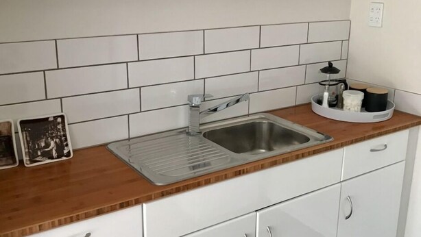 Una cocina con un lavamanos de acero inoxidable, armarios blancos y una encimera de madera.