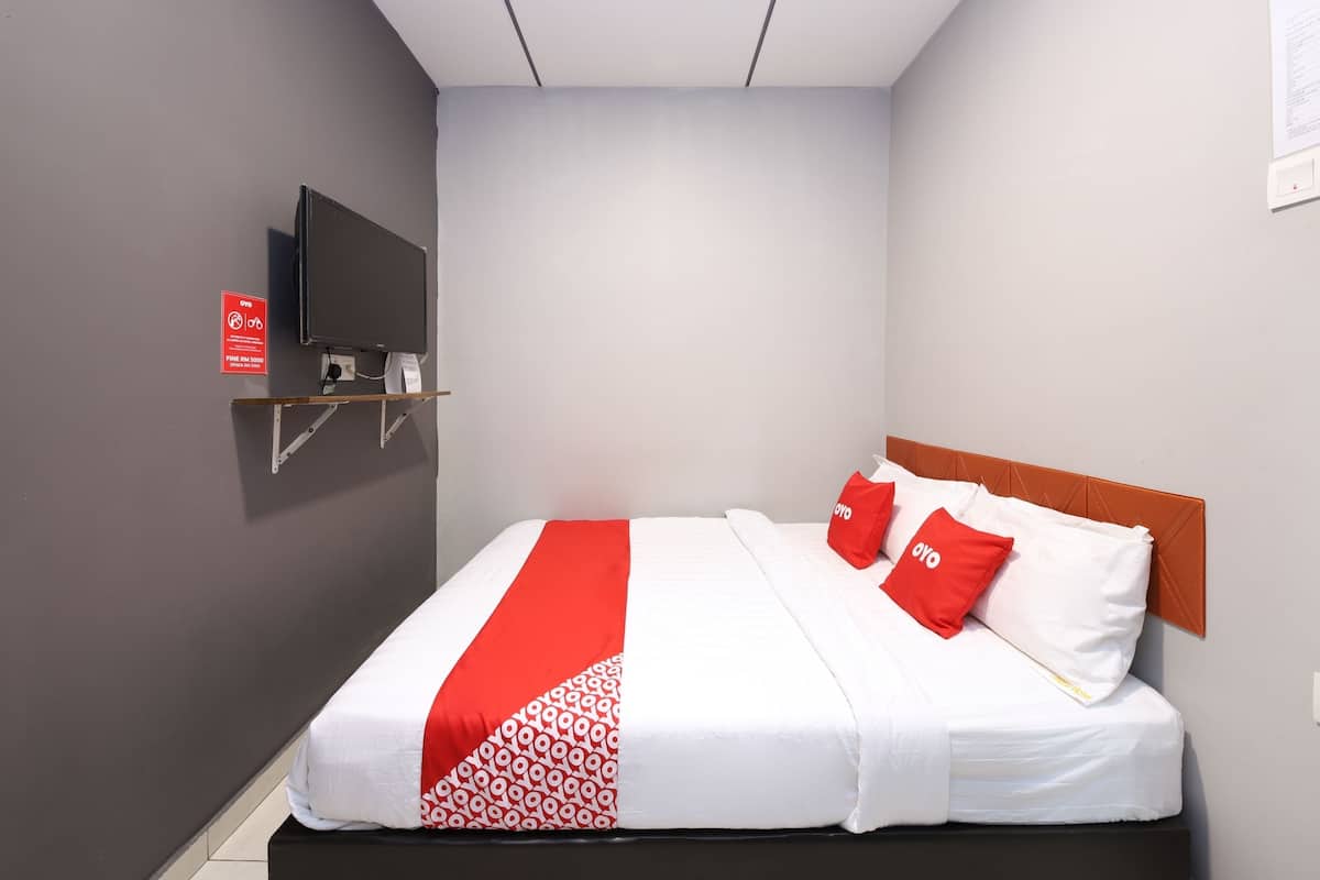 Quarto de hotel com cama, TV montada e colcha vermelha e branca.