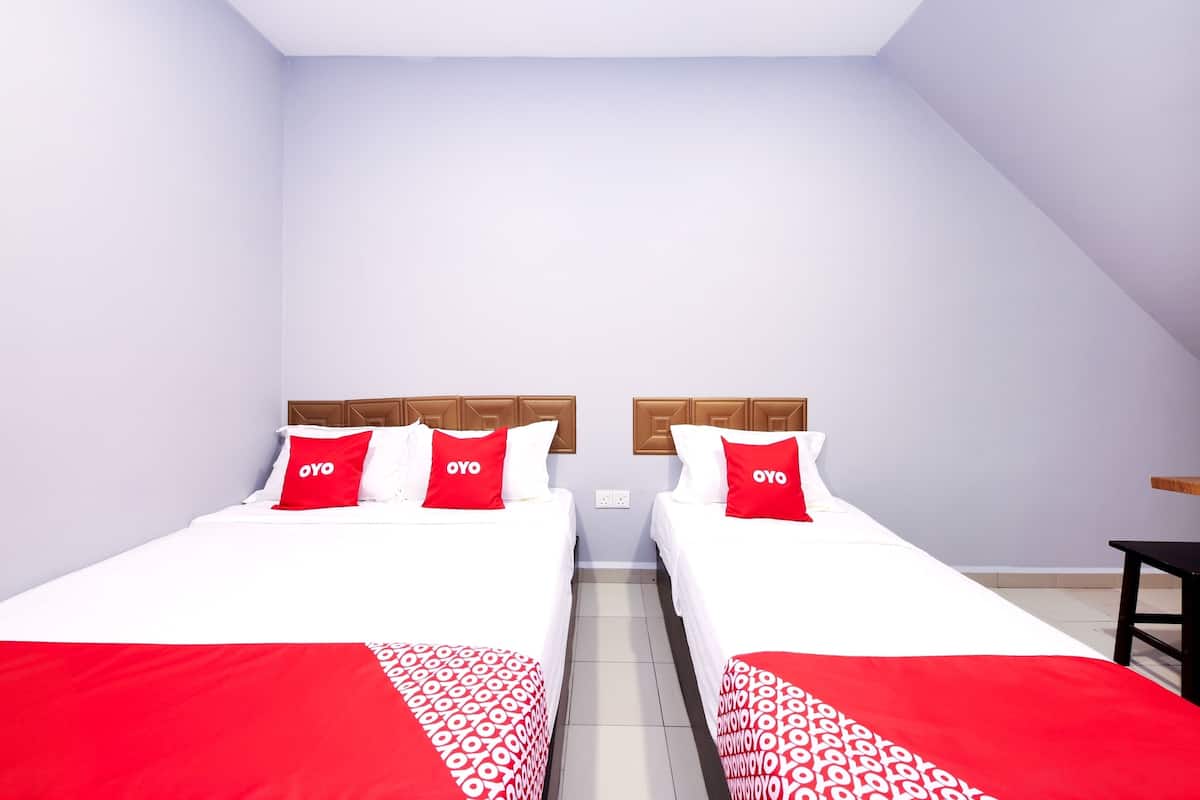 Quarto de hotel com duas camas, cada uma com colcha vermelha e branca, e cabeceira de madeira.