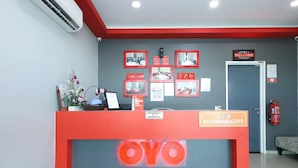A hotel reception area with a red counter, a welcome sign, framed pictures, and a fire extinguisher.