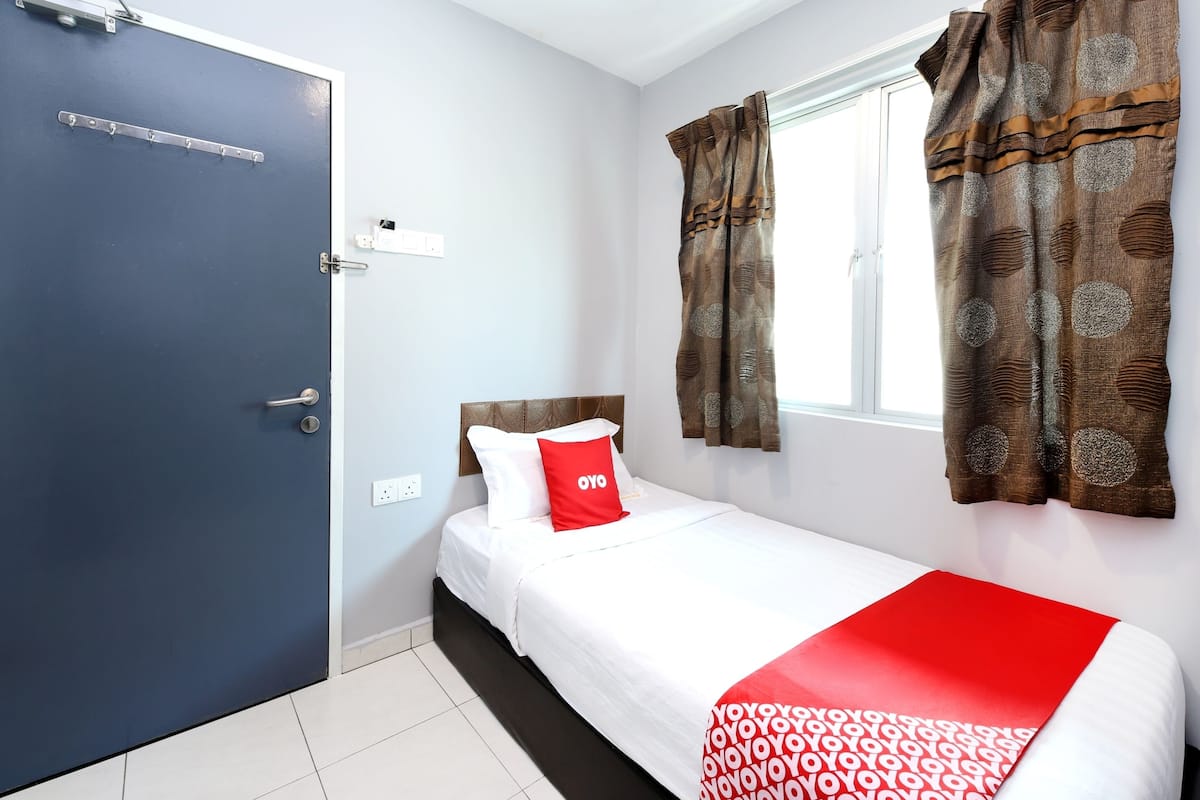 Quarto de hotel com cama, janela com cortinas, porta e luminária fixada na parede.