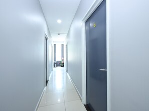 A clean, modern hallway with a blue door on the right and a trash bin in the center.