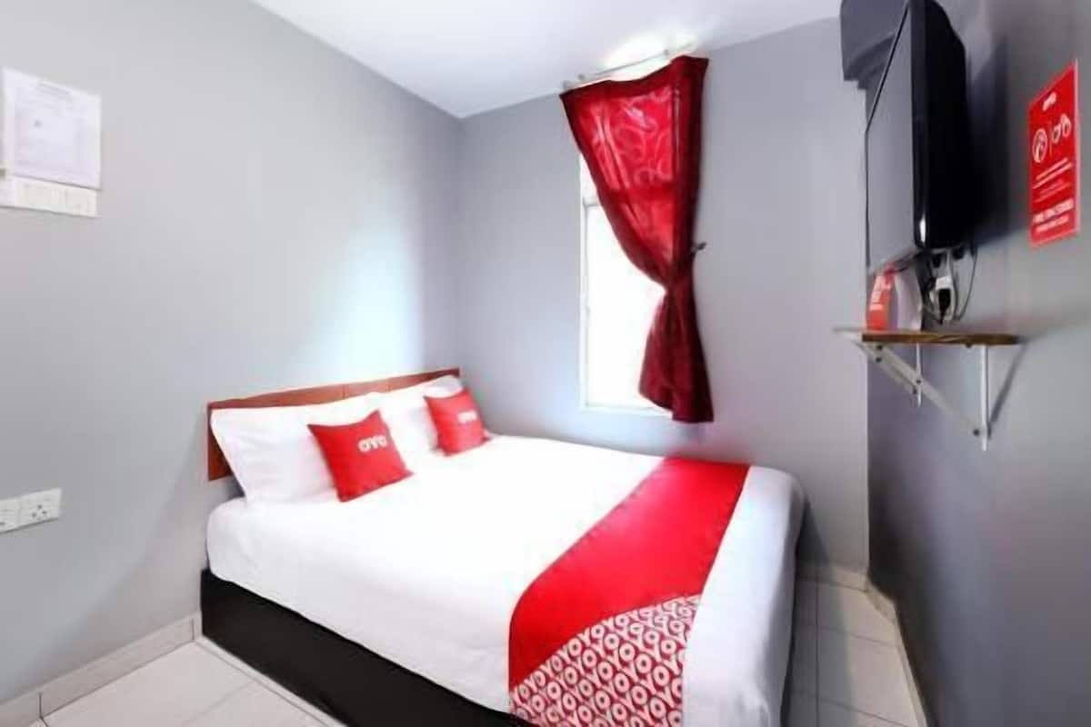 Uma cama com edredom branco e vermelho, dossel vermelho, televisão montada e placa vermelha na parede.