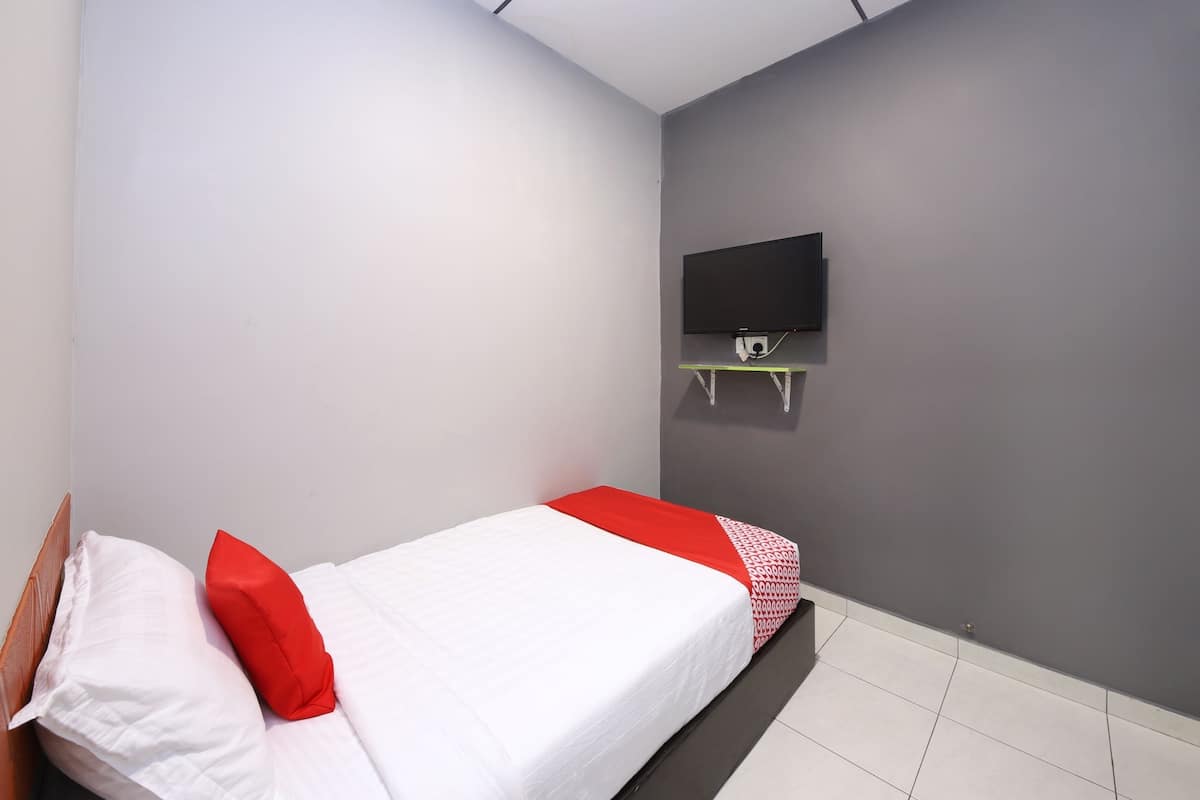 Quarto com uma cama, uma televisão fixada na parede e uma pequena prateleira.
