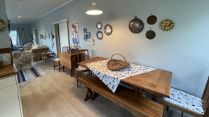 Un comedor con una mesa de madera y bancos, una cesta colgante y platos en la pared.