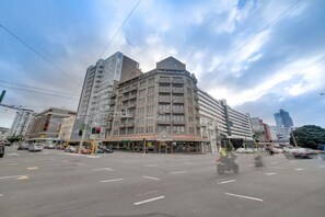 Un hotel de varios pisos con una entrada destacada en esquina, un área de estacionamiento y una intersección de calles.