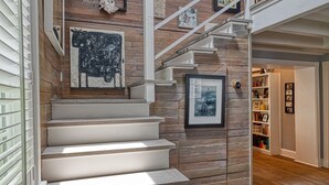 Una escalera de madera con barandilla blanca que conduce a un segundo piso con una estantería y cuadros enmarcados.