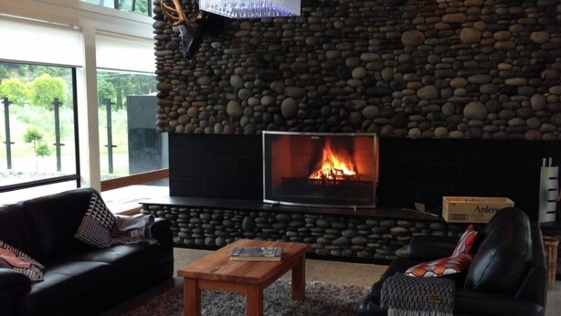 A living room with a stone wall, a fireplace, a black leather sofa, and a coffee table.