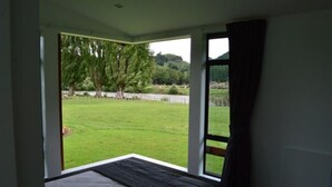 A bedroom with a large window, a bed, and a view of a grassy area and trees.