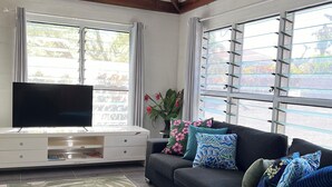 A living room with a black sofa, a flat-screen TV, and a ceiling fan. - Spacious 3 bedroom home, 10min to town. Unlimited Wifi & AC available! (Apia)