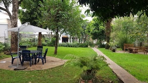 Un patio con mesa y sillas, rodeado de abundante vegetación y árboles.