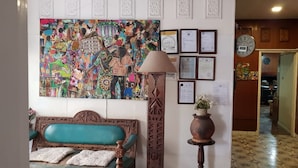 Un vestíbulo con un cuadro abstracto de colores, un sofá de madera, una lámpara, un jarrón con flores y certificados enmarcados en la pared.